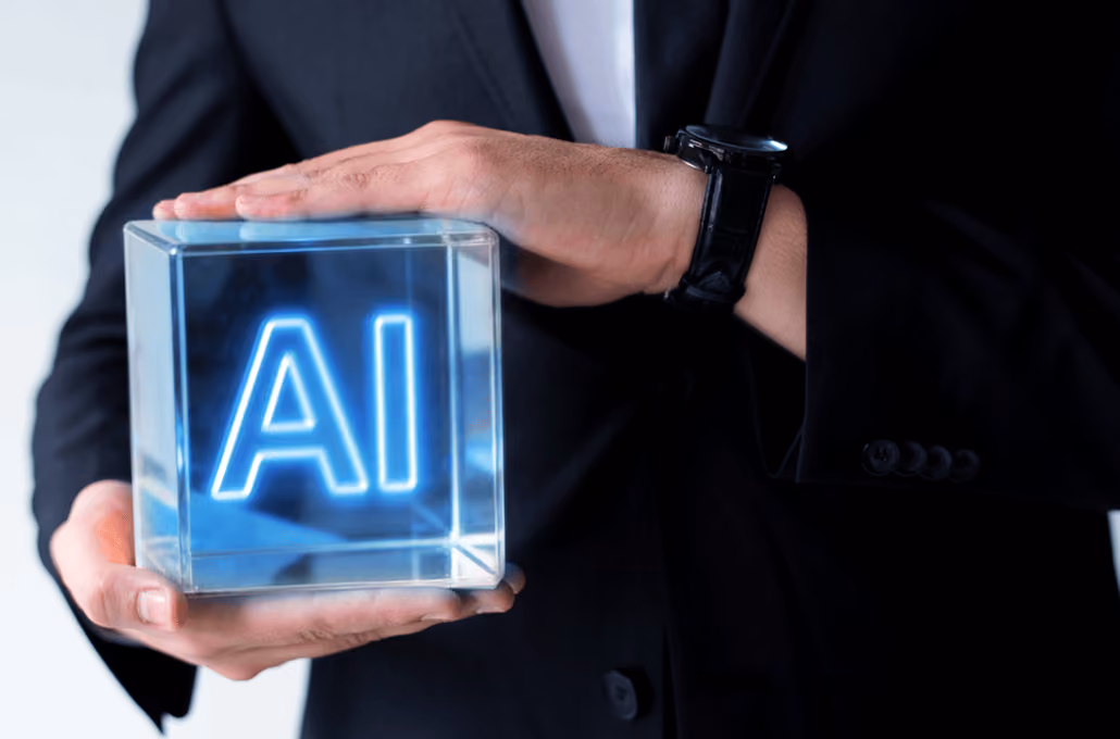 A person wearing a black suit jacket, holding a transparent, glowing glass cube with the letters "AI" illuminated in neon blue inside it.