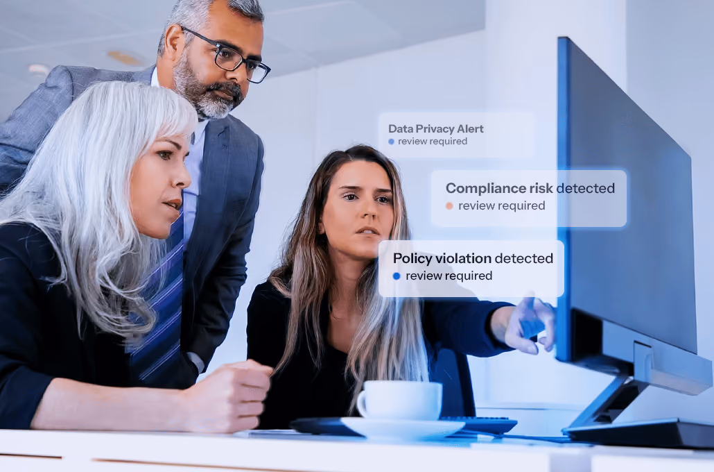 Three professional colleagues looking closely and with serious expressions at a computer monitor in an office setting.