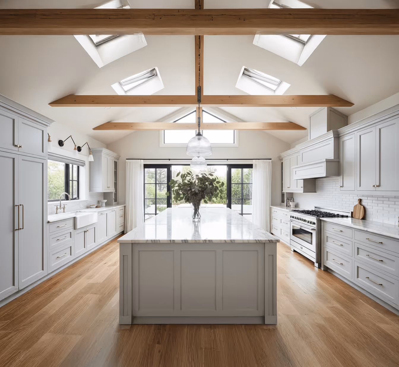 Bright modern kitchen with large marble island, wooden beams, skylights, and black-framed glass doors.
