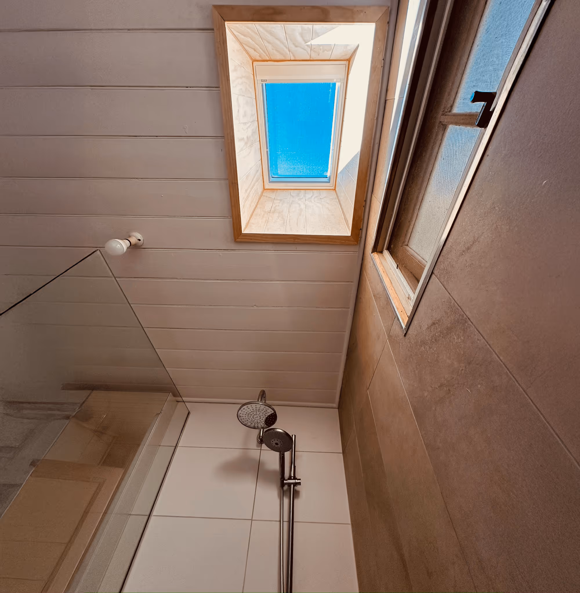 Interior of a bright room with a skylight, wall-mounted air conditioner, glass door leading outside, and a modern red umbrella stand casting shadows.