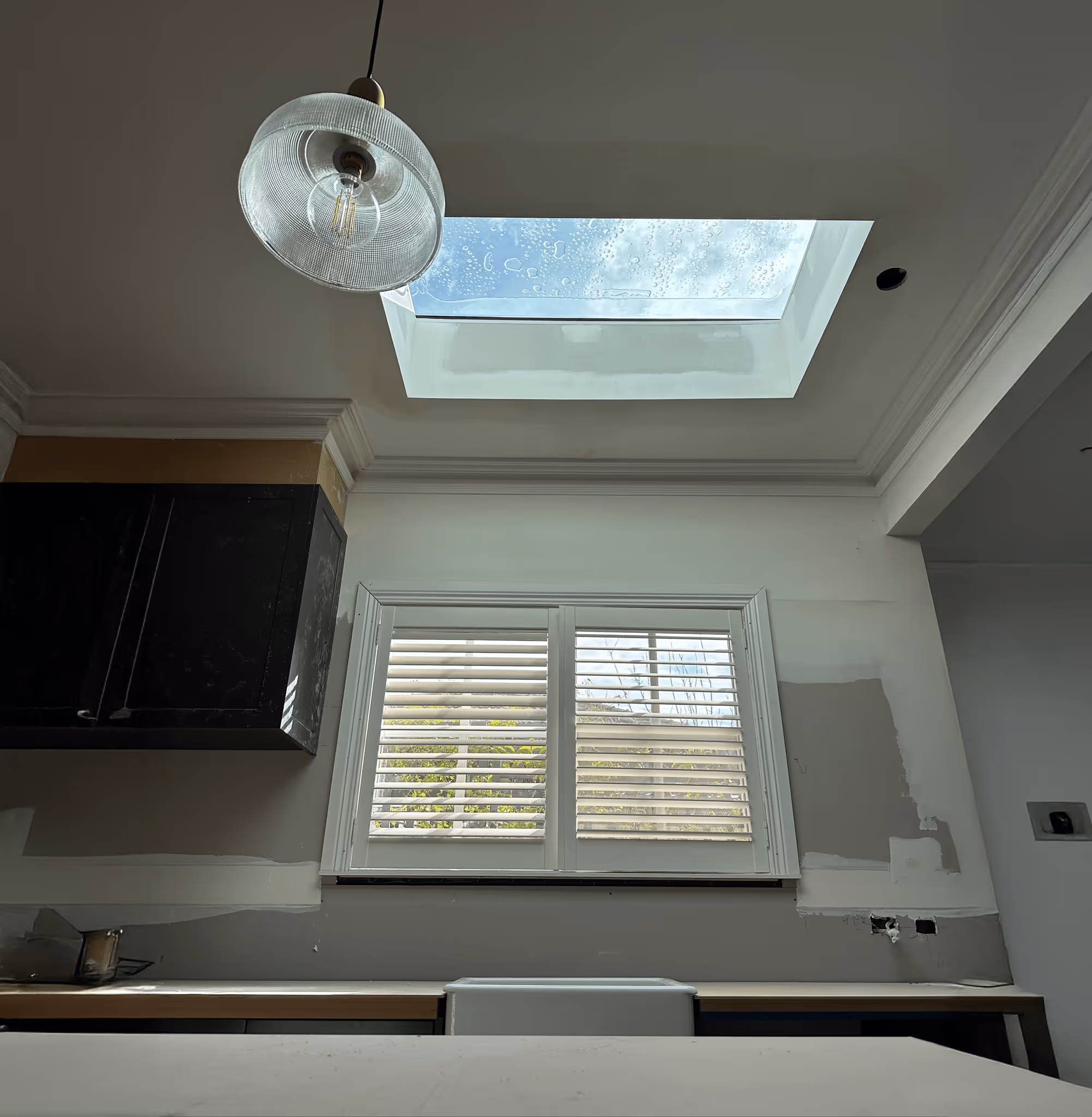 Corrugated metal rooftop with a rectangular skylight reflecting clouds, with modern twin cylindrical skyscrapers and a blue sky in the background.