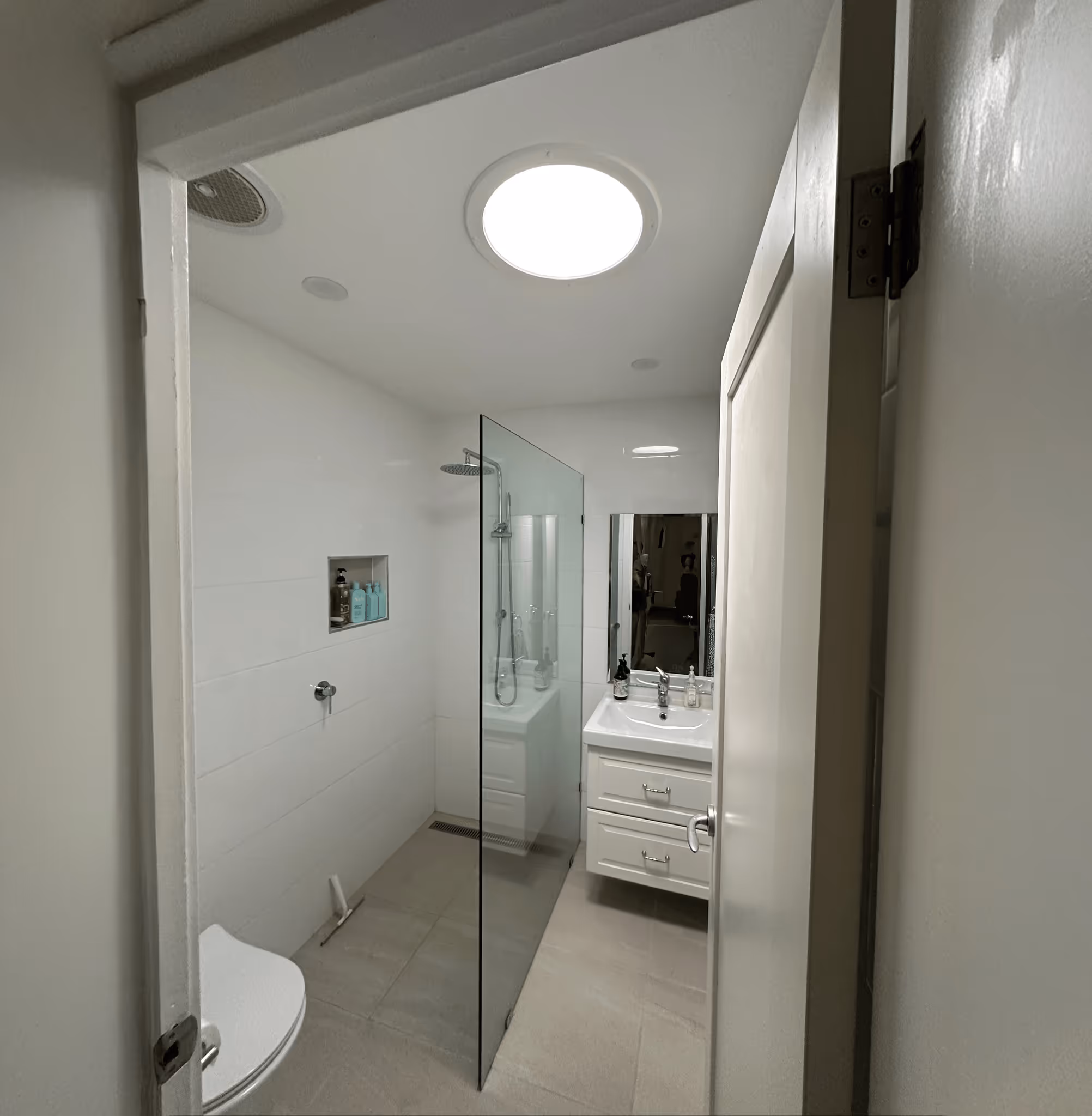 Small modern bathroom with a glass shower divider, white vanity with sink and mirror, and a white toilet partially visible.