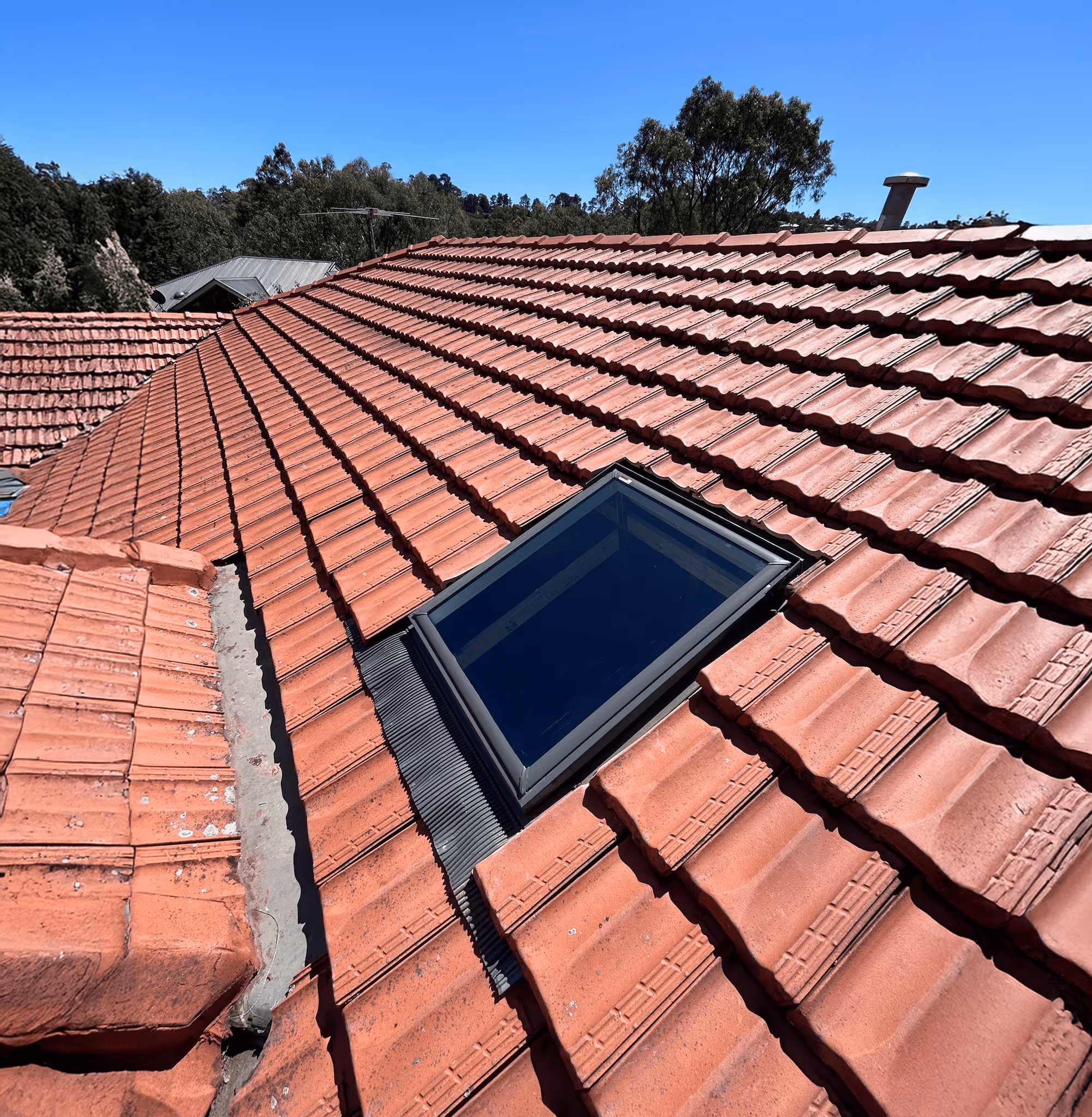 Rectangular skylight installed on a red tiled roof under a clear blue sky.