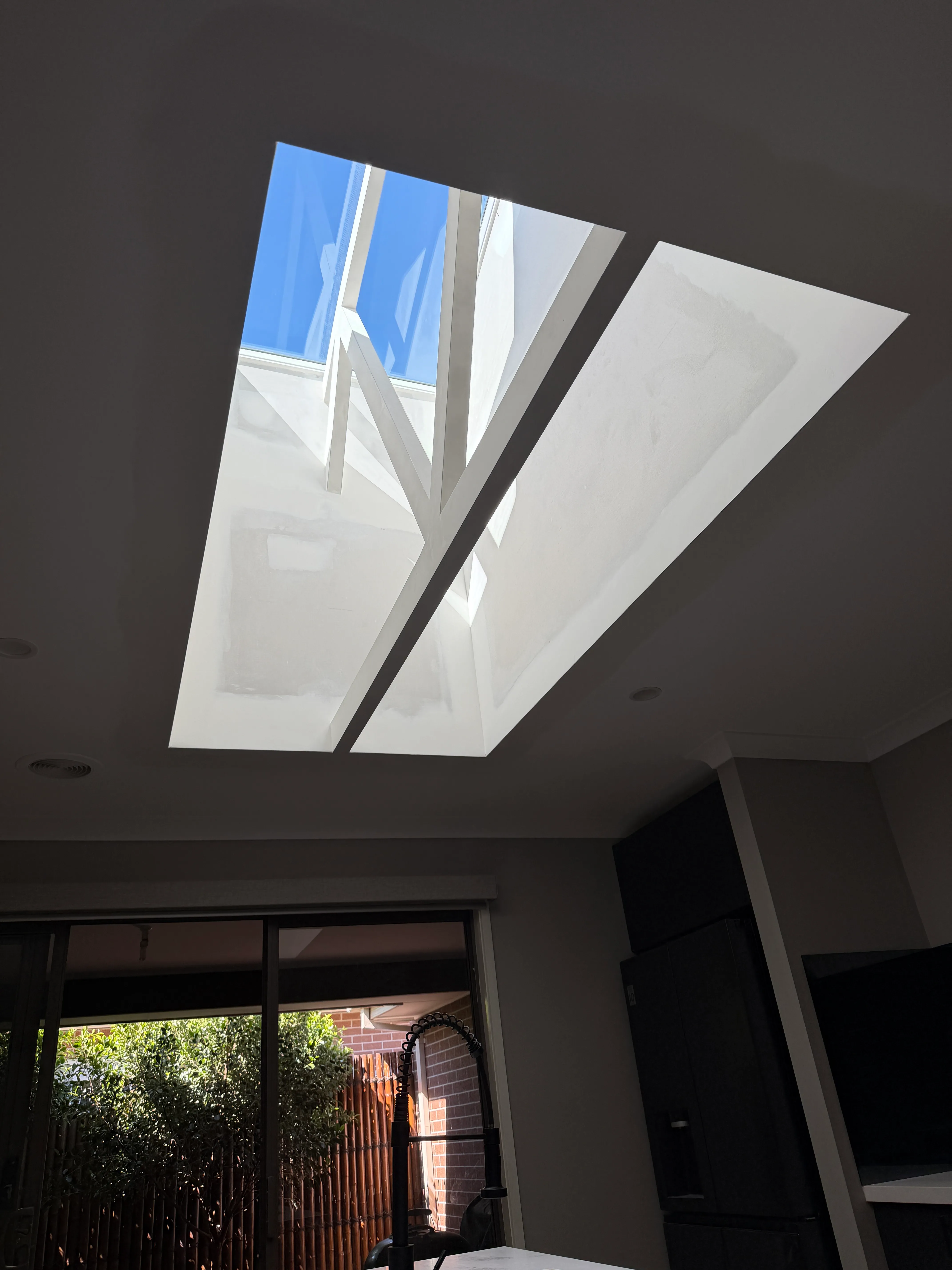 Minimalist living room with beige sofa, floral pillow, wooden side table, and skylight windows in slanted ceiling.