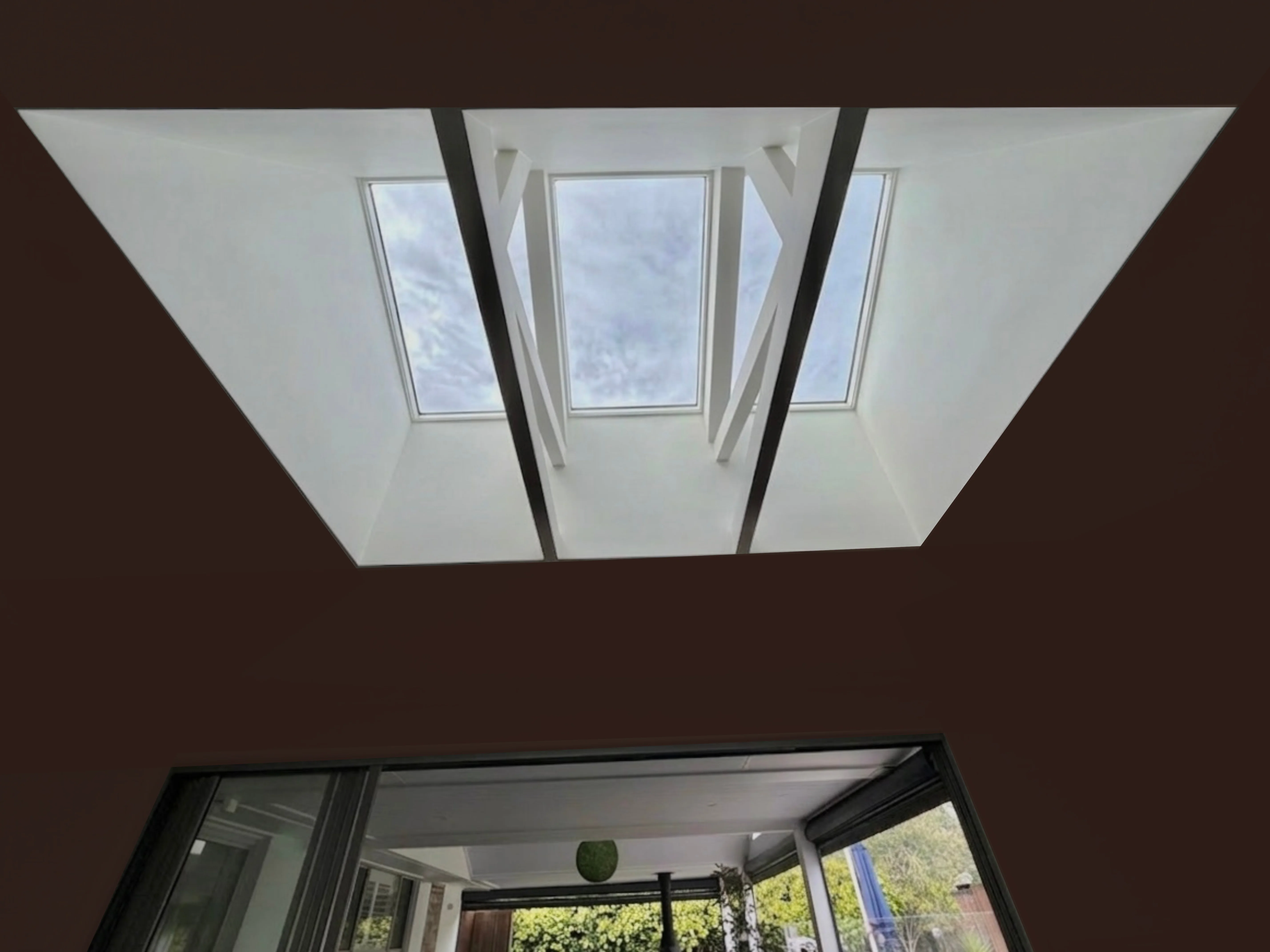 Bright modern kitchen with gray cabinets, central island, wooden dining table and chairs, a large plant, and open glass doors leading to a green garden.