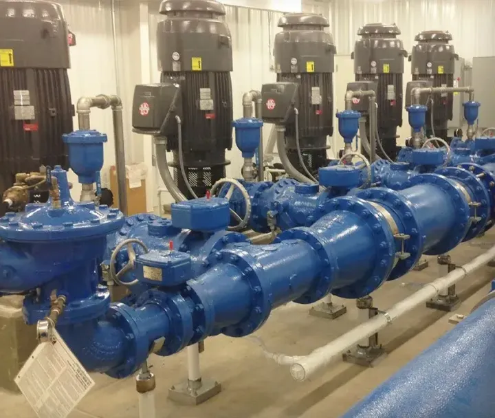 Multiple large blue industrial water pumps connected in a row with black motors in a clean indoor mechanical room.