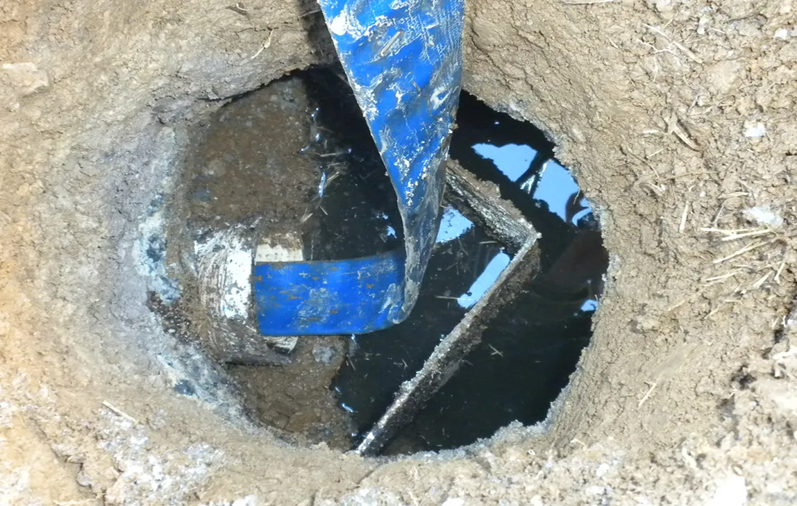 Close-up of a blue hose inserted into a muddy hole filled with water and dirt.