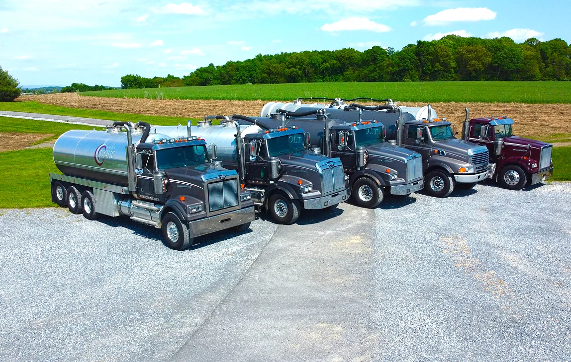 Five large tanker trucks parked in a row on gravel.