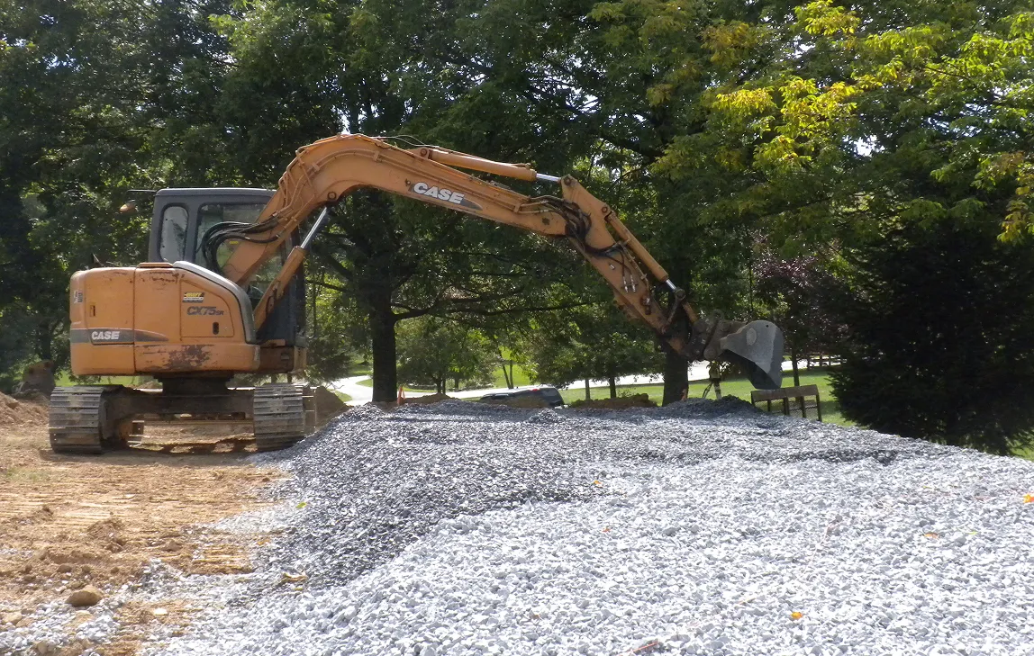Yellow CASE excavator with a large arm digging and moving gravel at a construction site.