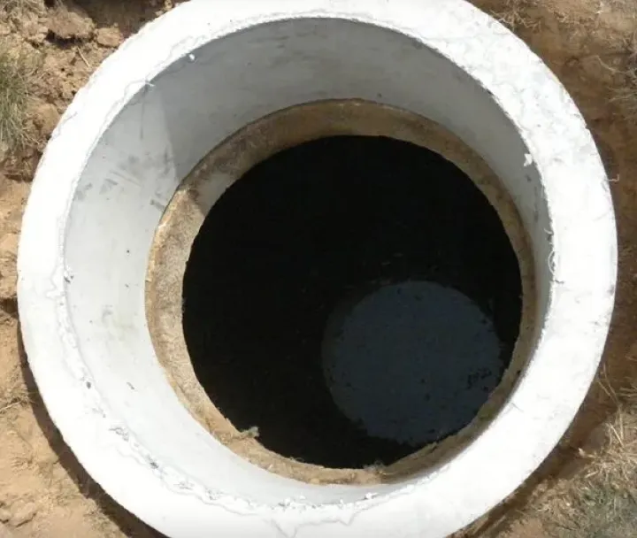 Top view of an open concrete well surrounded by soil.