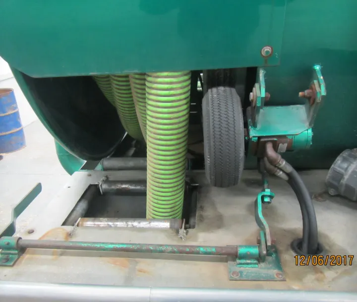 Close-up of industrial equipment with green corrugated hoses, a black tire, and metal components on a concrete floor.