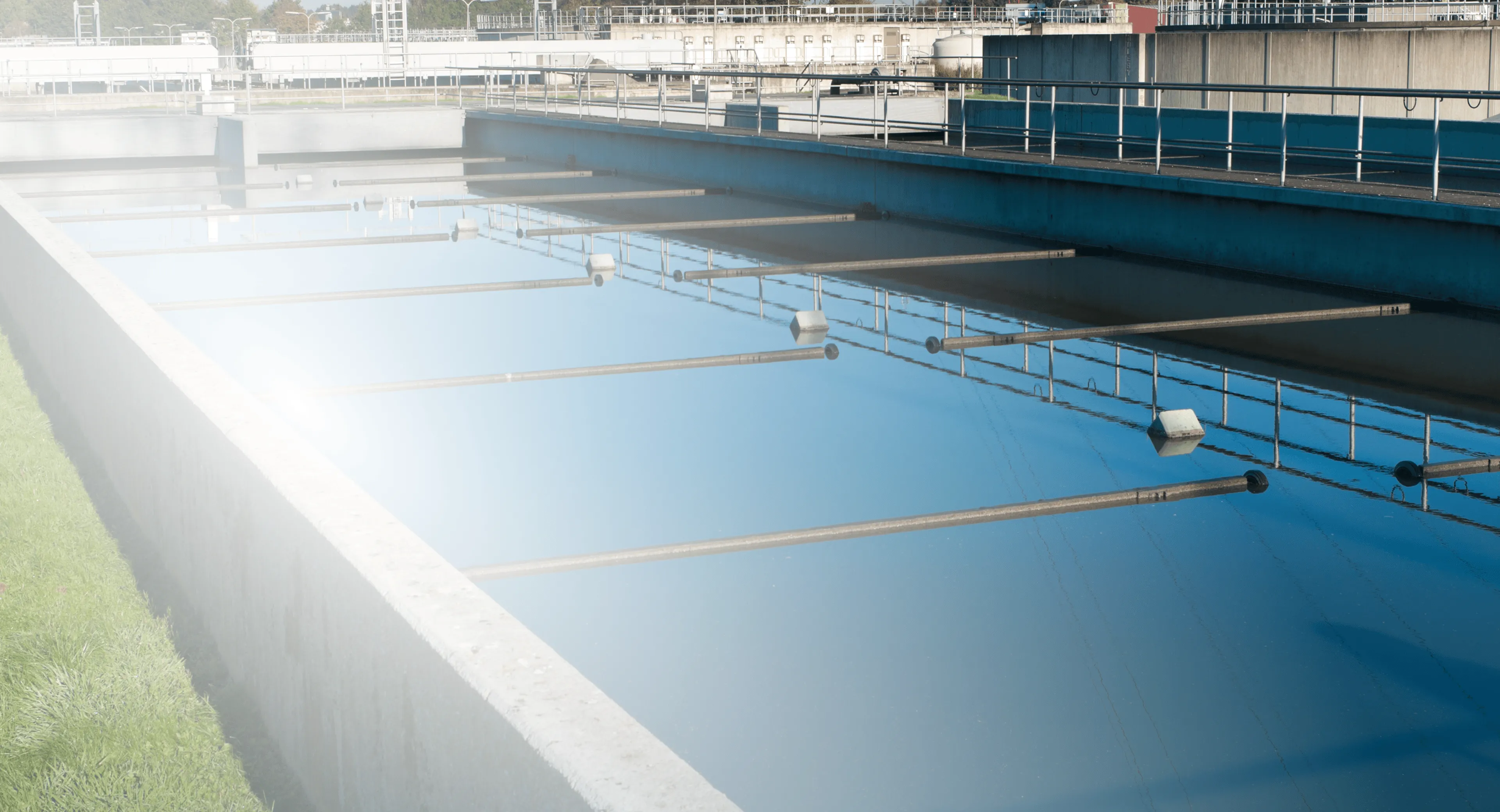 Water treatment facility basin with clear blue water and suspended aeration pipes.