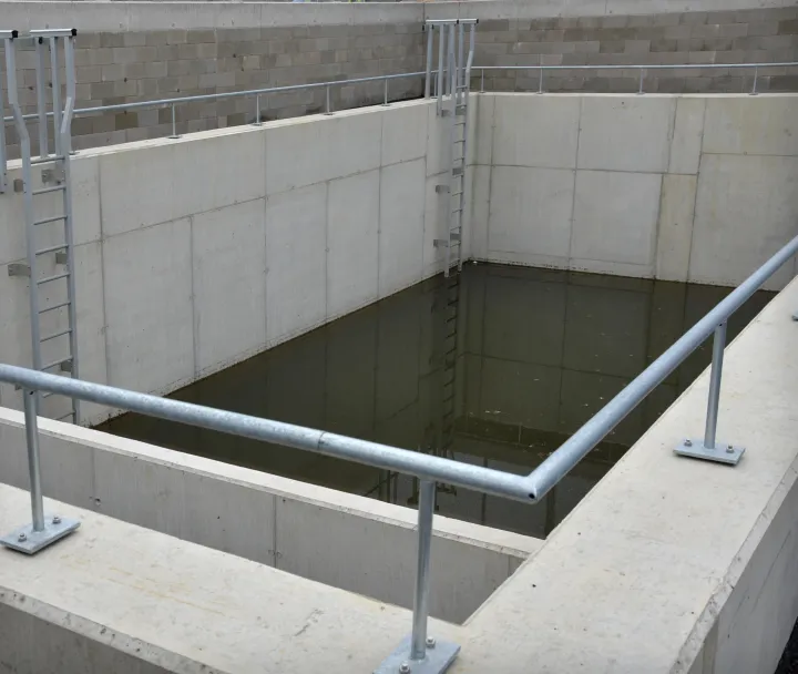 Empty concrete water reservoir with metal railings and ladders inside a brick-lined area.