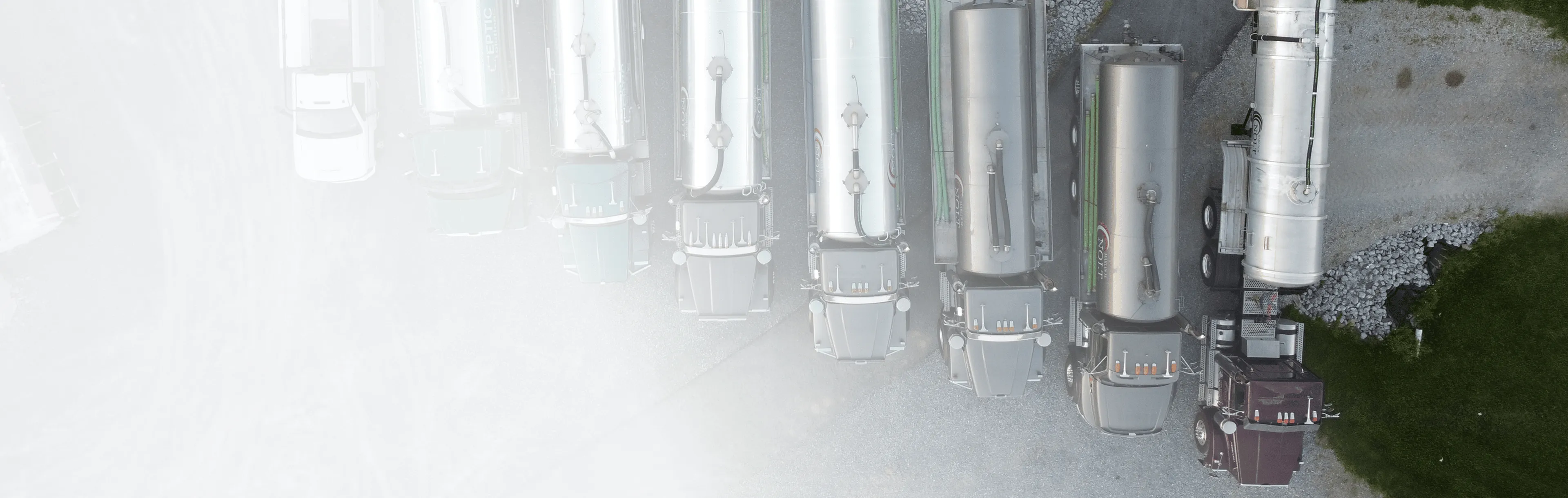 Aerial view of several tanker trucks and a white utility truck parked on gravel.