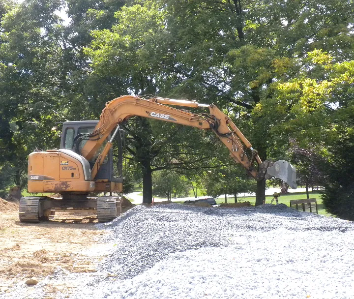 Yellow CASE excavator with a large arm digging and moving gravel at a construction site.