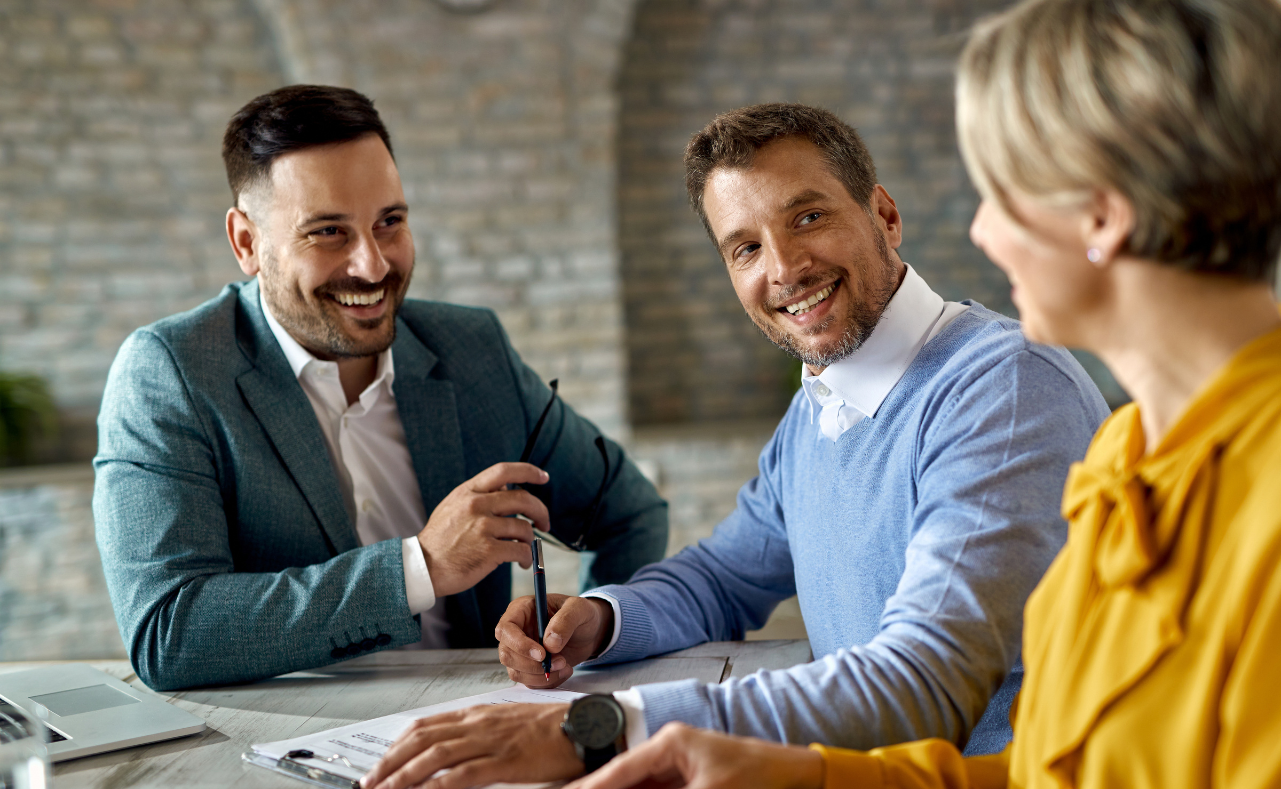 Three professionals smiling and engaging in a business meeting at a desk.