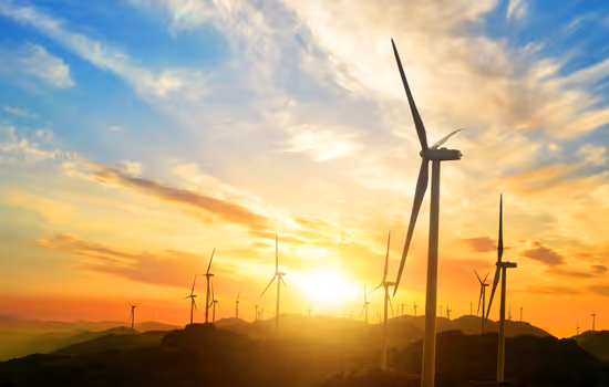 Large wind turbines in a field at sunset representing renewable energy.