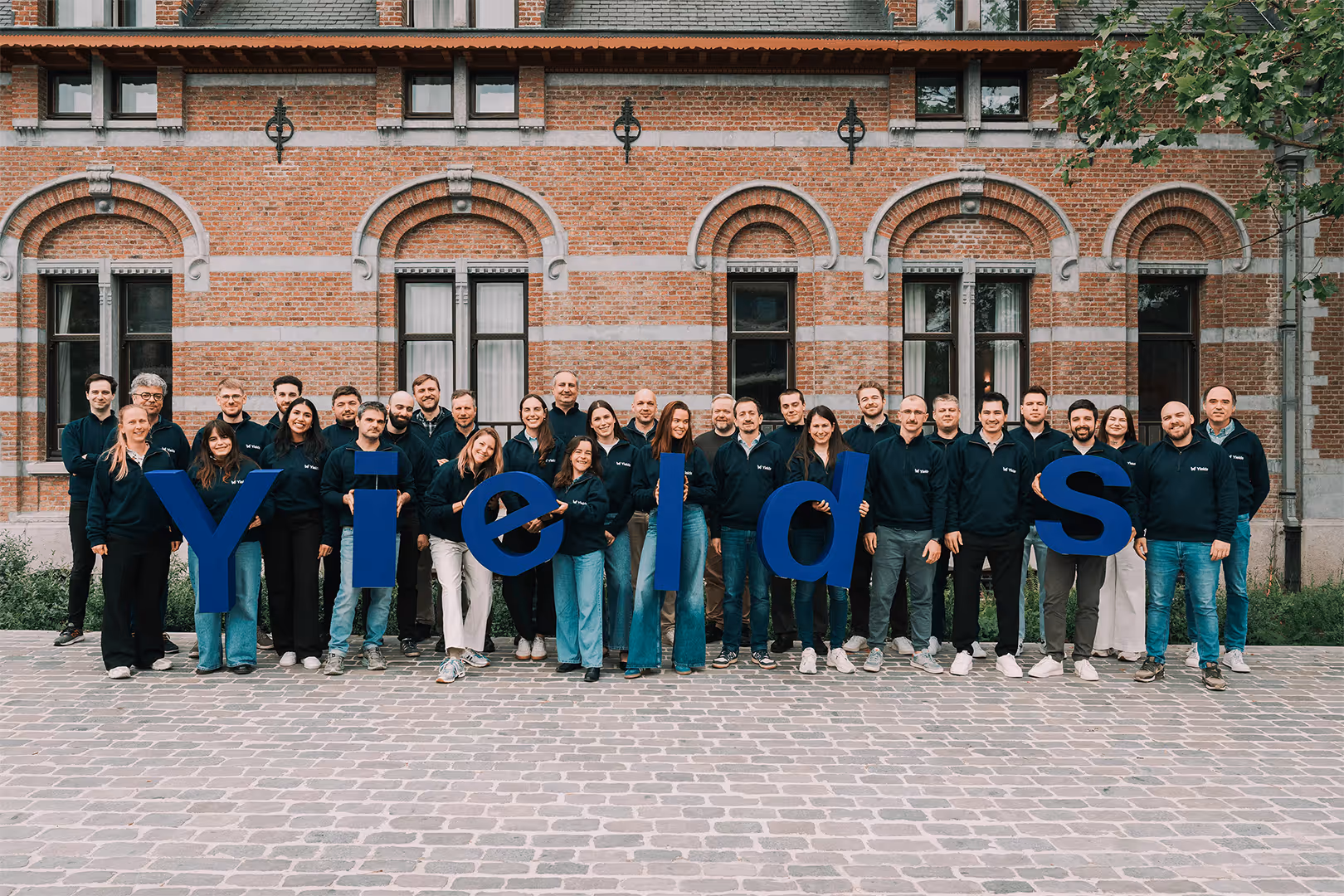 Group of people standing in front of a brick building holding large blue letters spelling 'yields'.