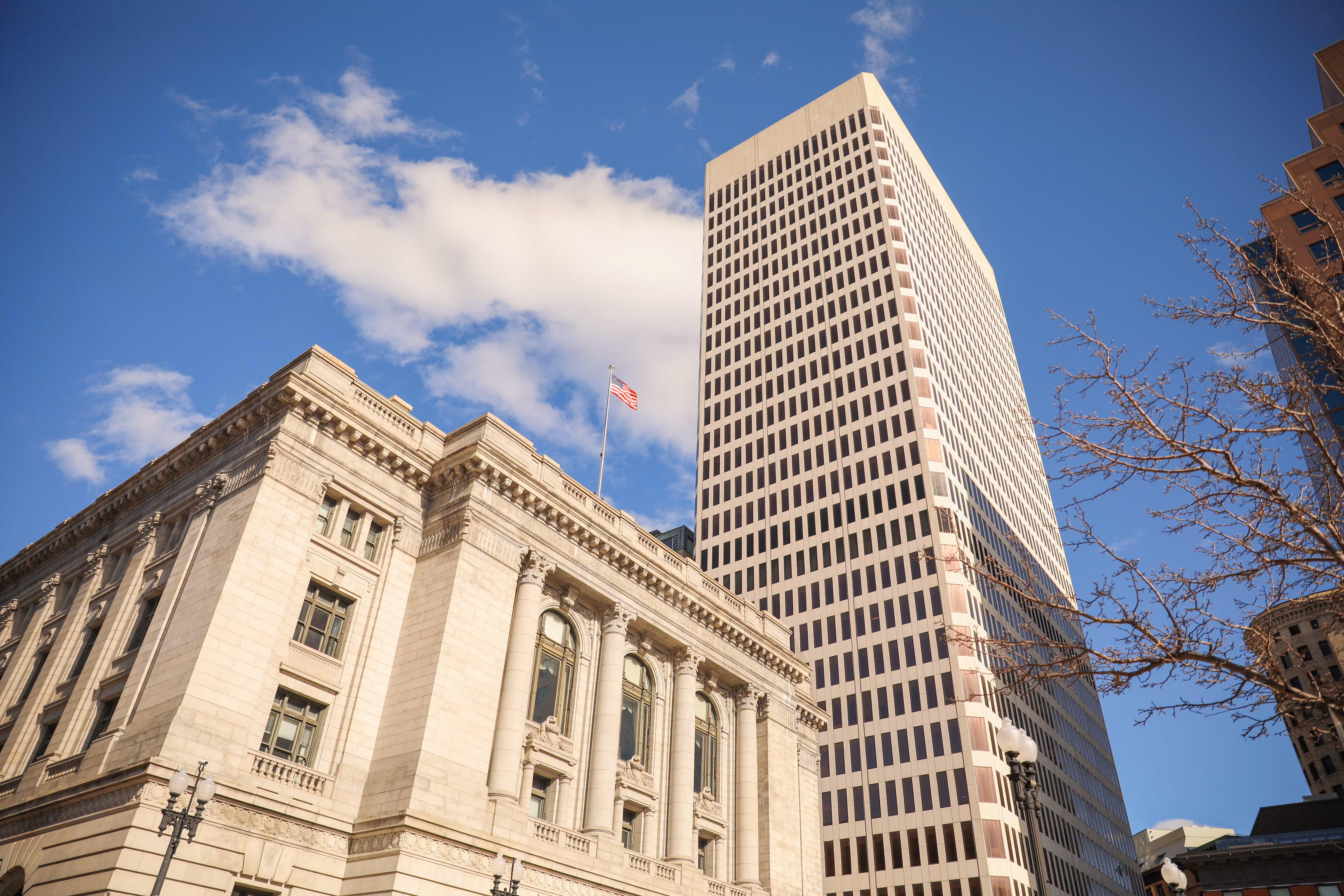 The United States flag flying between a historic civic building and a modern office tower in a US downtown