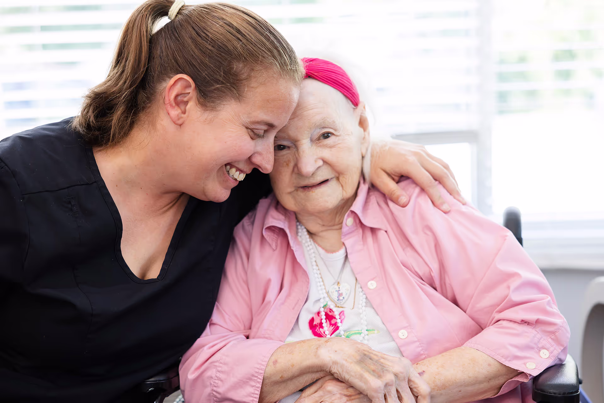Staff member hugging elderly woman in a wheel chair close up