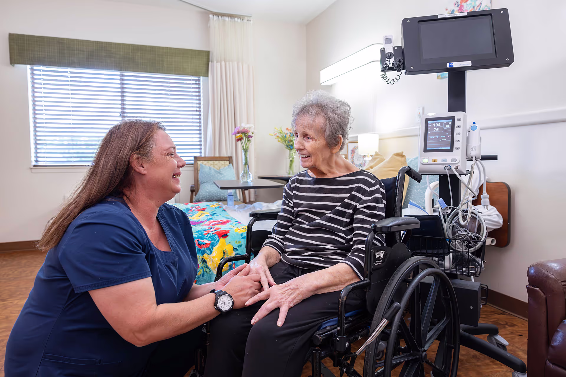 a CNA speaks with an elderly woman in a wheel chair