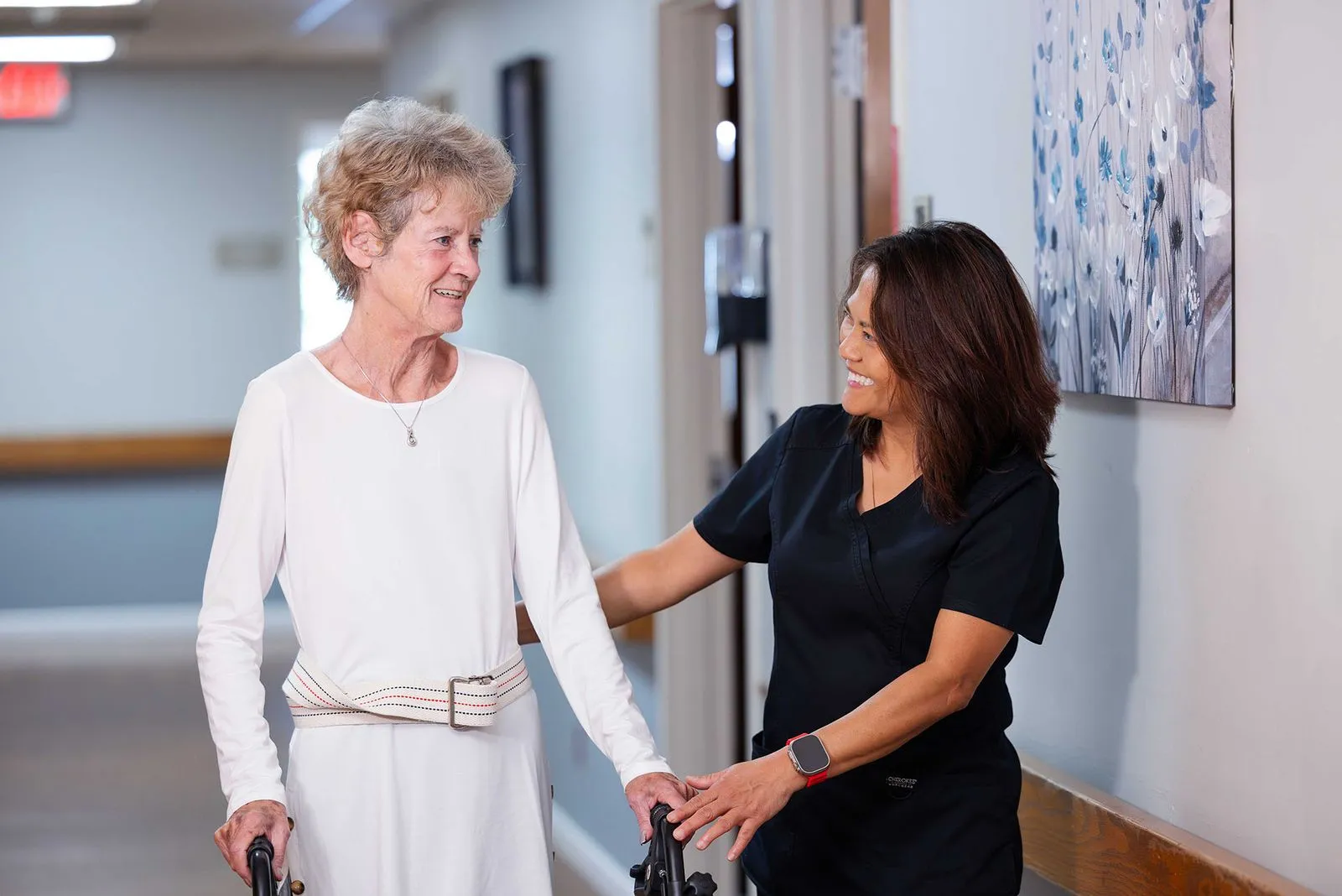 Happy staff member assisting elderly woman walking down the hallway