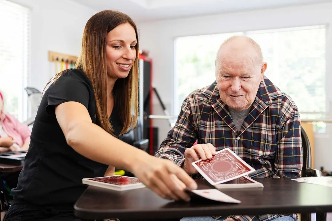 Occupational therapist and elderly man in a wheel chair playing a card game