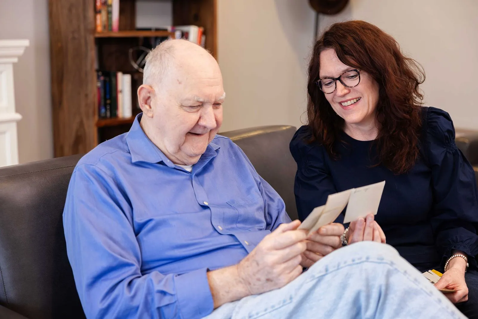 Daughter and elderly father smiling while looking at old photos on the couch