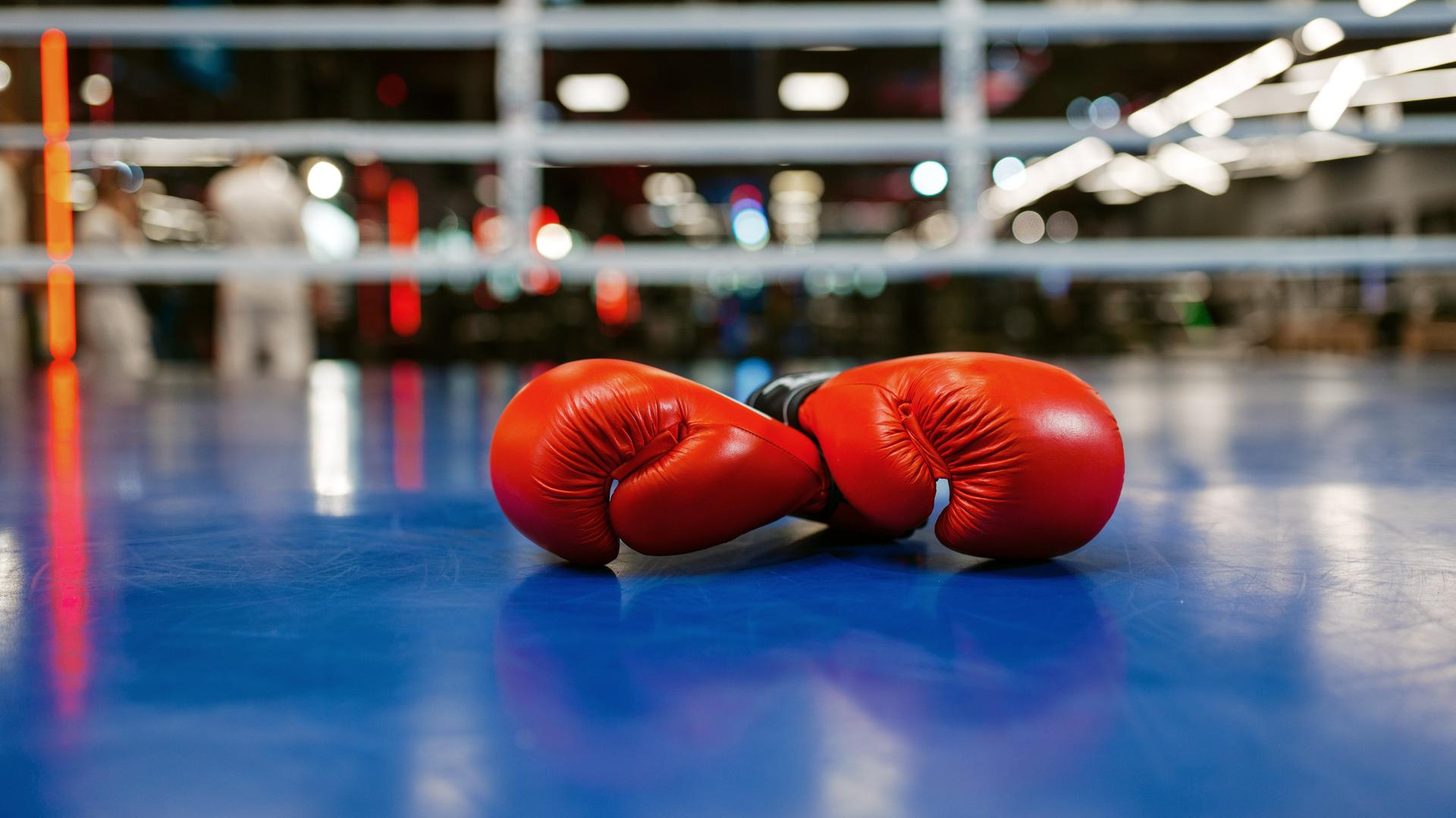 Man in a black turtleneck and orange knit beanie looking to the side with arms crossed outdoors.