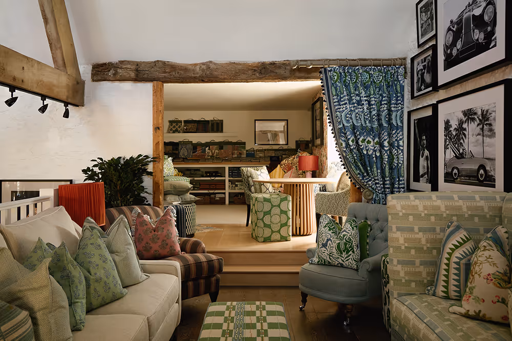 Cozy living room with patterned pillows, a mix of upholstered chairs and sofas, wooden beams, and framed black-and-white photographs on the wall.