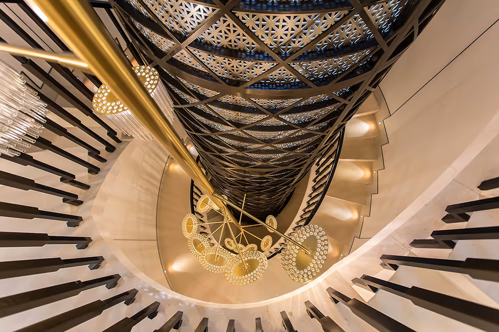 View looking down a spiral staircase with ornate black metal, white steps, and a modern chandelier with circular lights.