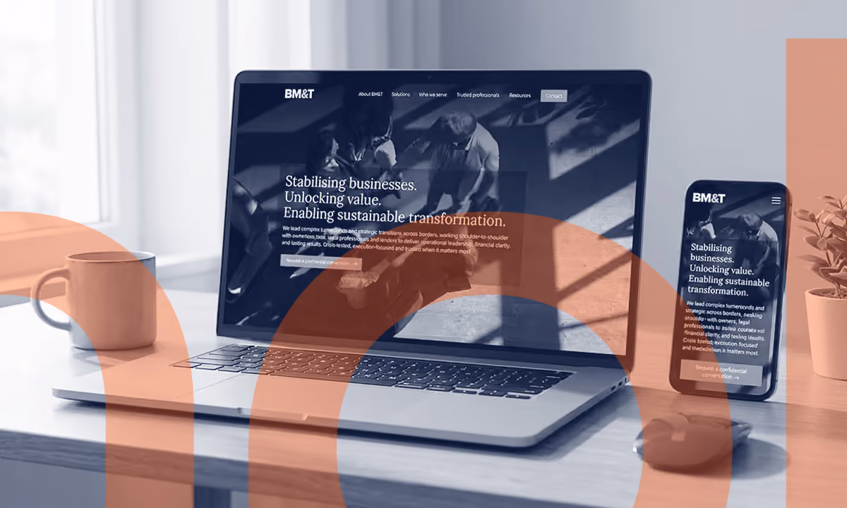 Laptop and smartphone on a wooden desk displaying BM&T website with text about stabilizing businesses and enabling sustainable transformation.