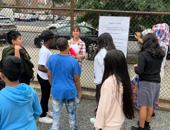 Teacher addressing a group of students outdoors near a sign