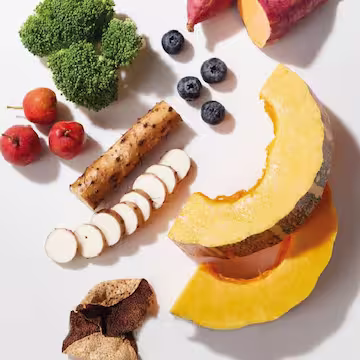 Variety of fresh fruits and vegetables including broccoli, blueberries, sliced yam, sliced root vegetable, persimmons, and two pumpkin slices on a white surface.
