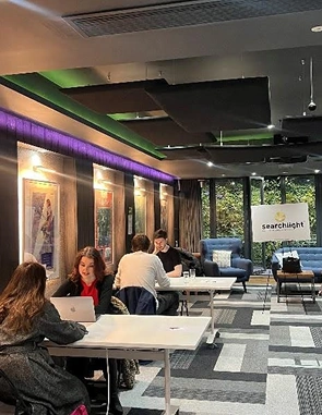 People working on laptops and talking in a modern office lounge with a sign reading 'searchlight'.