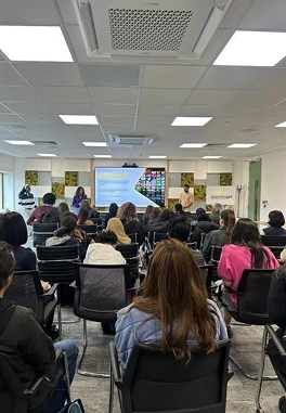 People seated in rows facing a speaker presenting slides in a bright conference room.