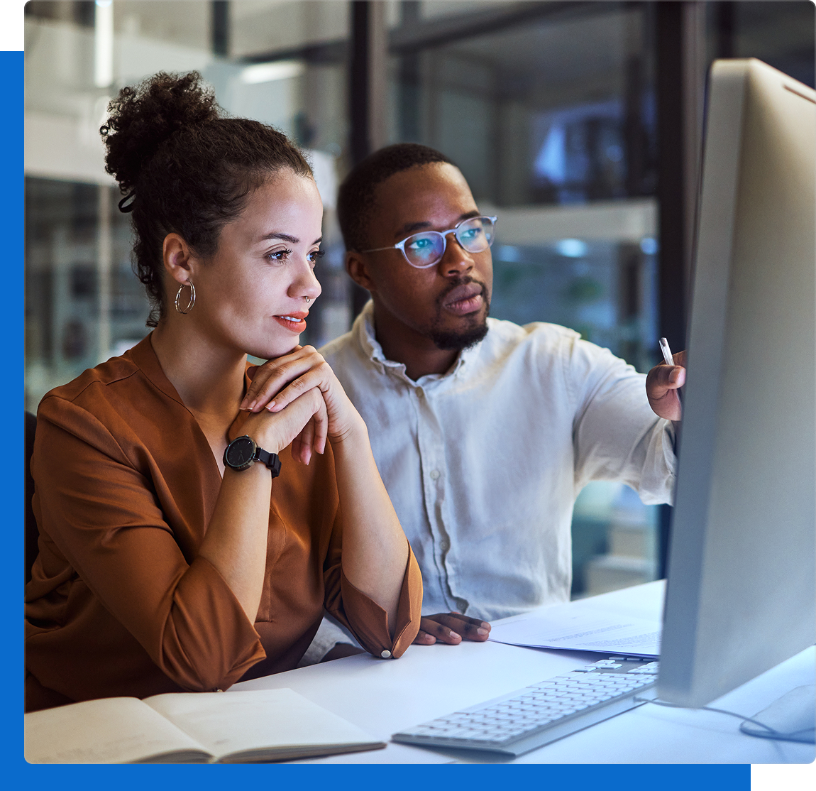 Two colleagues, a woman and a man, attentively looking at a computer screen in a modern office.