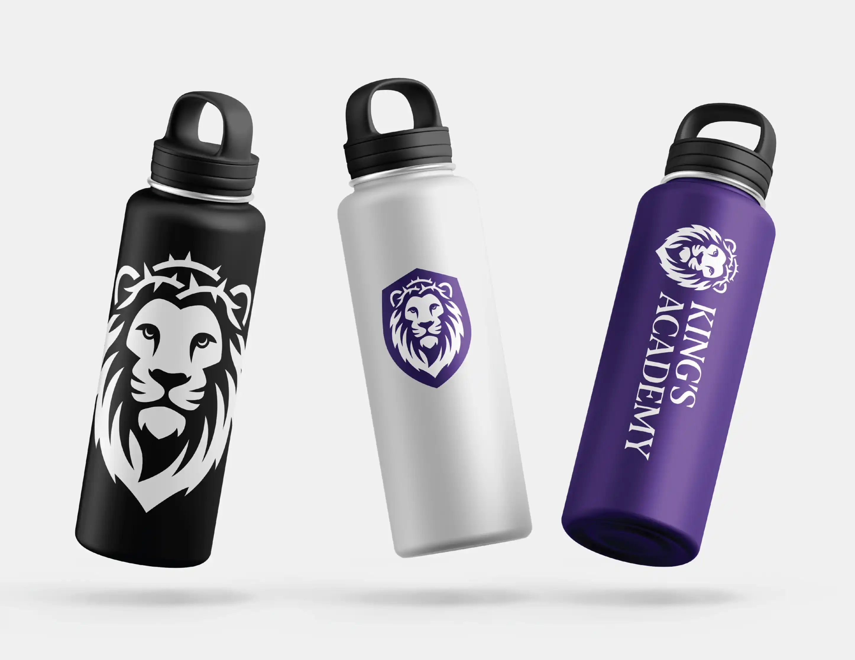 Three insulated water bottles in black, white, and purple, each featuring a lion logo and 'KING'S ACADEMY' text on the purple bottle.