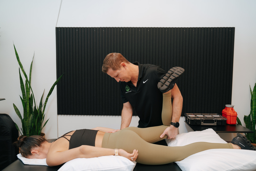 Physiotherapist stretching the leg of a woman lying face down on a treatment table. Tropic Athlete