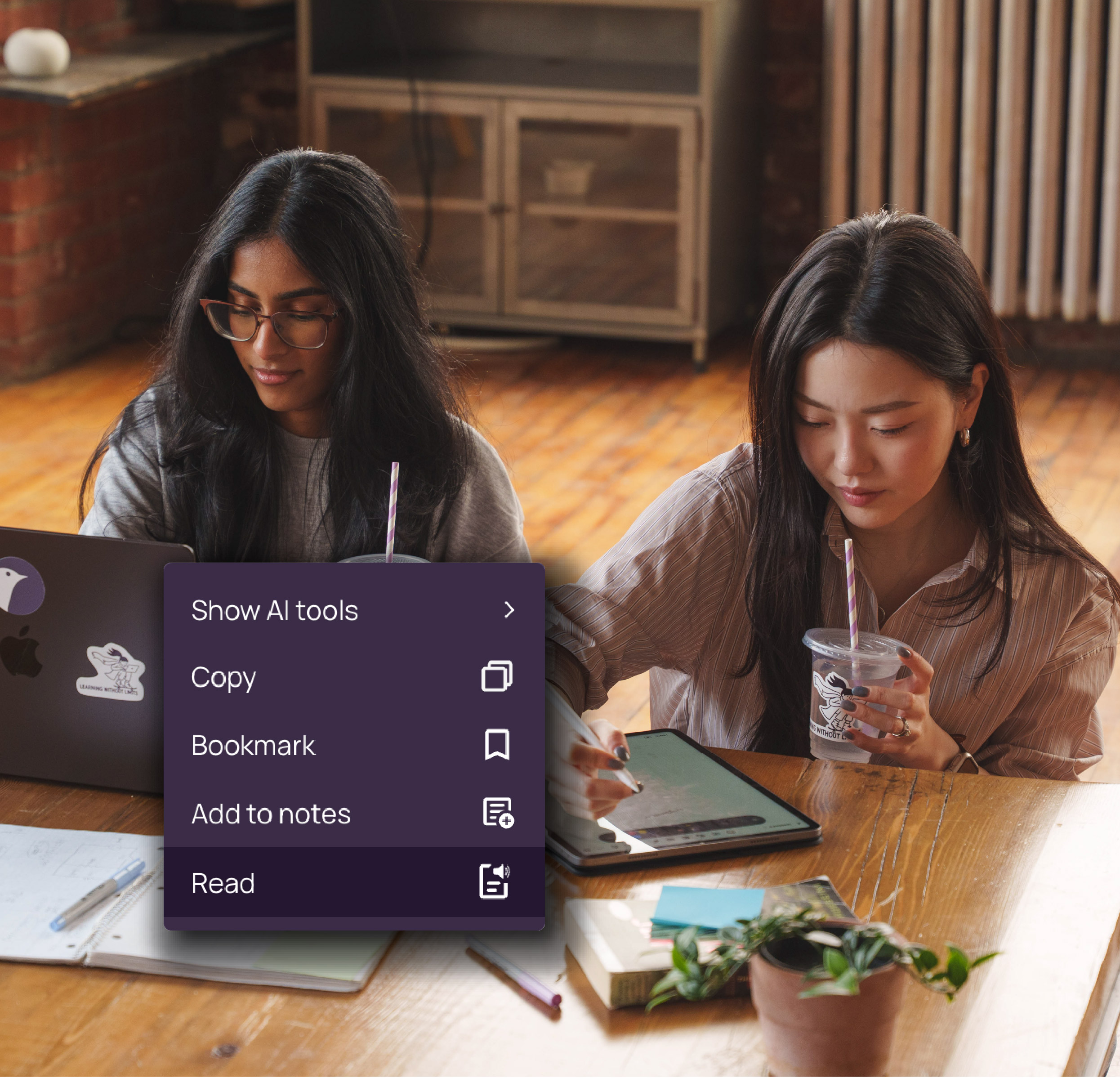 Two women working at a wooden table with a laptop and tablet, while a menu overlay displays options like Show AI tools, Copy, Bookmark, Add to notes, and Read.