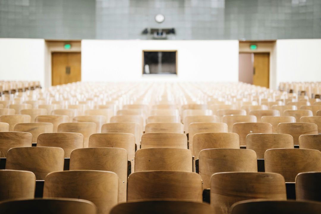 Empty rows of wooden chairs in an auditorium.