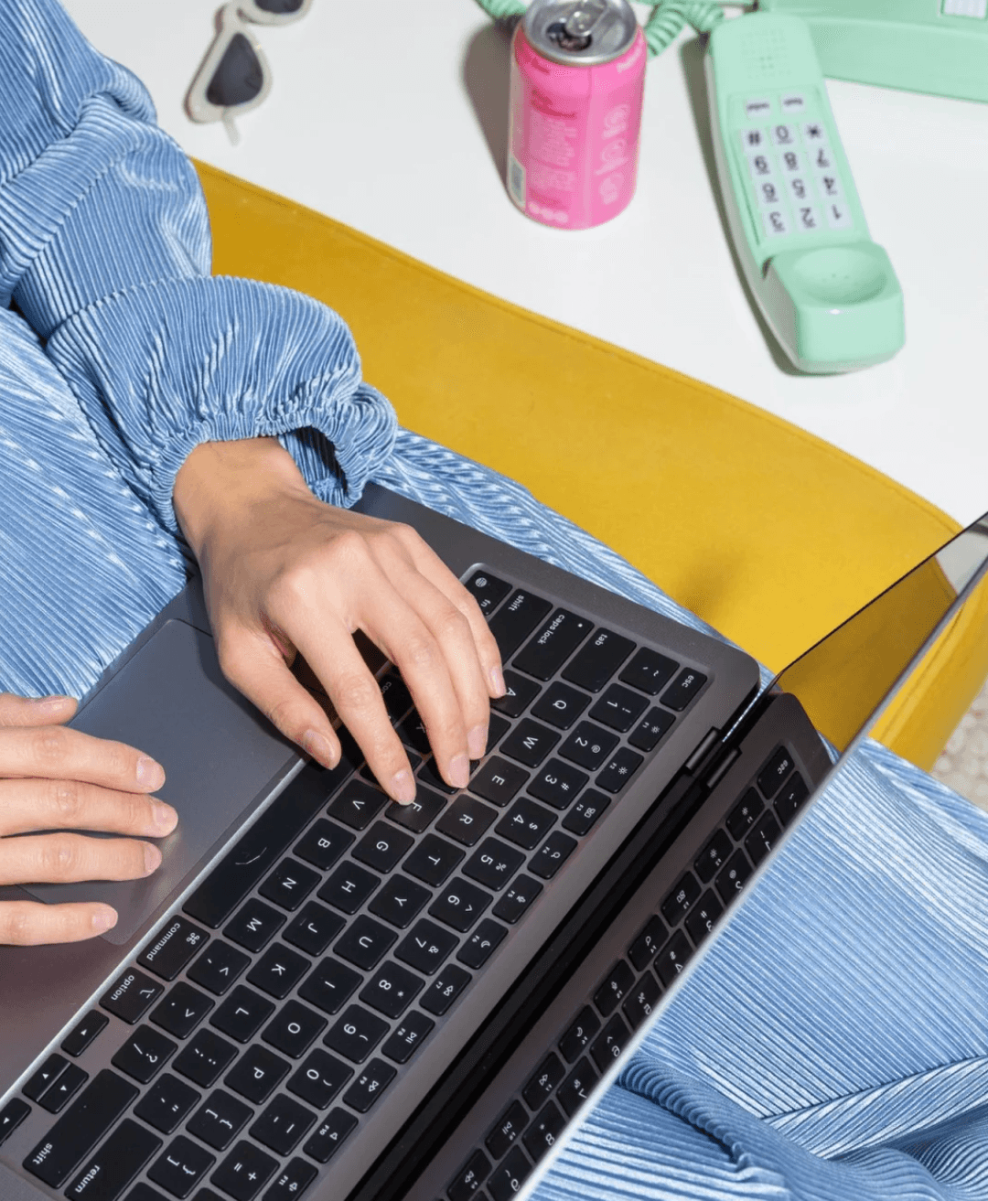A person in a blue dress on a yellow chair, typing on a laptop.