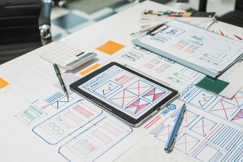 A table featuring papers, pens, and IPads, working on User Interface design for an application.