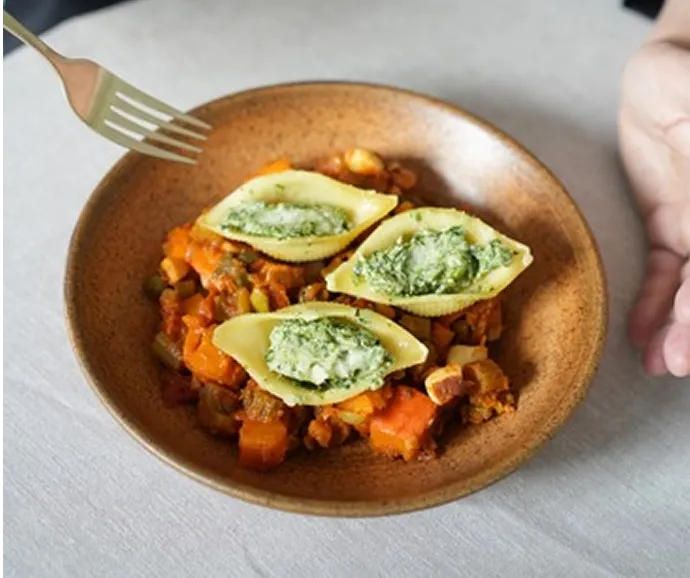Assiette gastronomique de pâtes farcies au fromage servies sur un mélange de légumes mijotés dans un concept de traiteur raffiné et créatif.