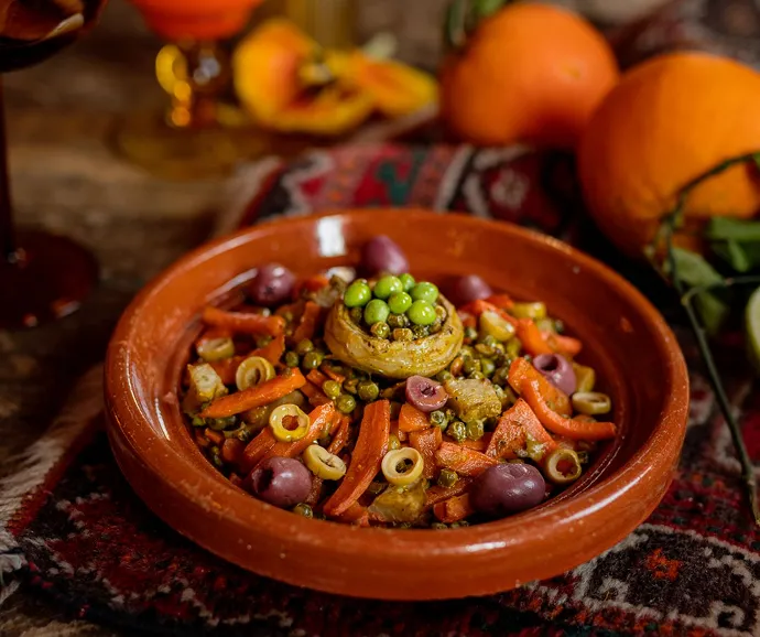 Plat traditionnel de légumes mijotés aux olives et petits pois servi dans une assiette en terre cuite dans un concept de traiteur aux saveurs authentiques.