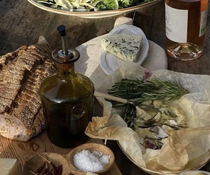 Composition gastronomique rustique avec fromage bleu, huile d’olive, pain artisanal et herbes fraîches présentés sur une table en bois dans un contexte de dégustation raffinée.