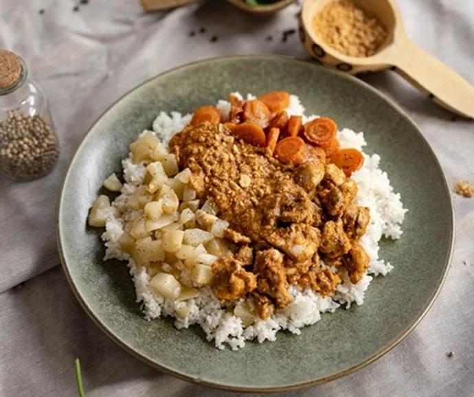 Assiette de riz garnie de poulet mijoté, légumes et sauce onctueuse présentée dans un concept de traiteur aux saveurs authentiques et réconfortantes.