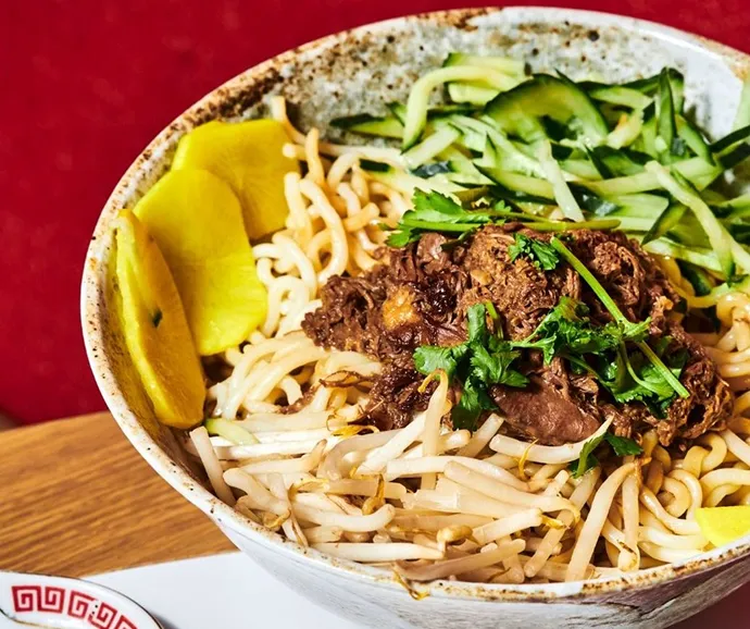 Bol de nouilles asiatiques garnies de bœuf braisé, concombre frais et légumes marinés, présenté dans un style street food gourmand et équilibré.