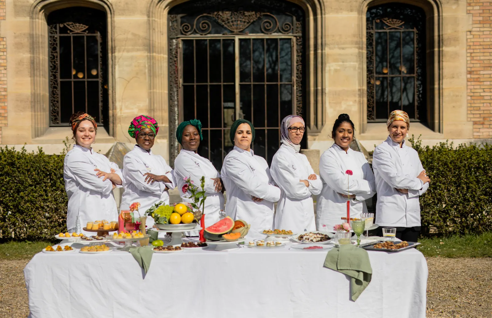 Sept cheffes en veste blanche derrière une table de buffet en plein air
