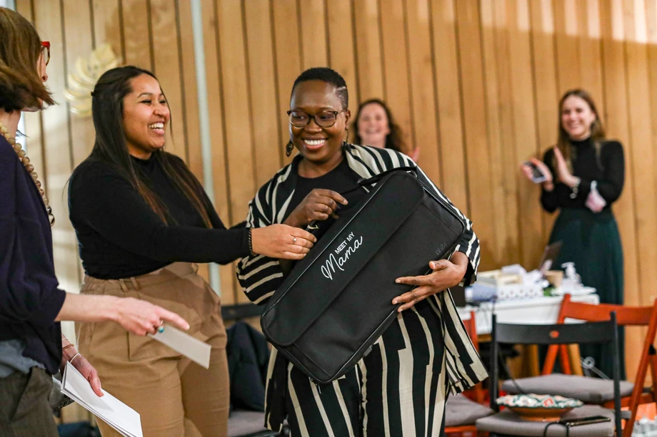 Une main verse une boisson rose rafraîchissante dans un verre sur une table élégante en extérieur, entourée de fruits, de fleurs et de plats colorés, illustrant une ambiance conviviale et estivale.